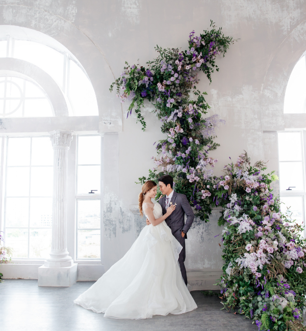 bride and groom standing under large purple flower arch